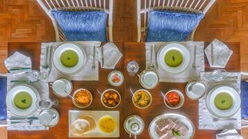 A dining table set for two with various dishes, including green soup and curry, arranged on white plates with gold rims.