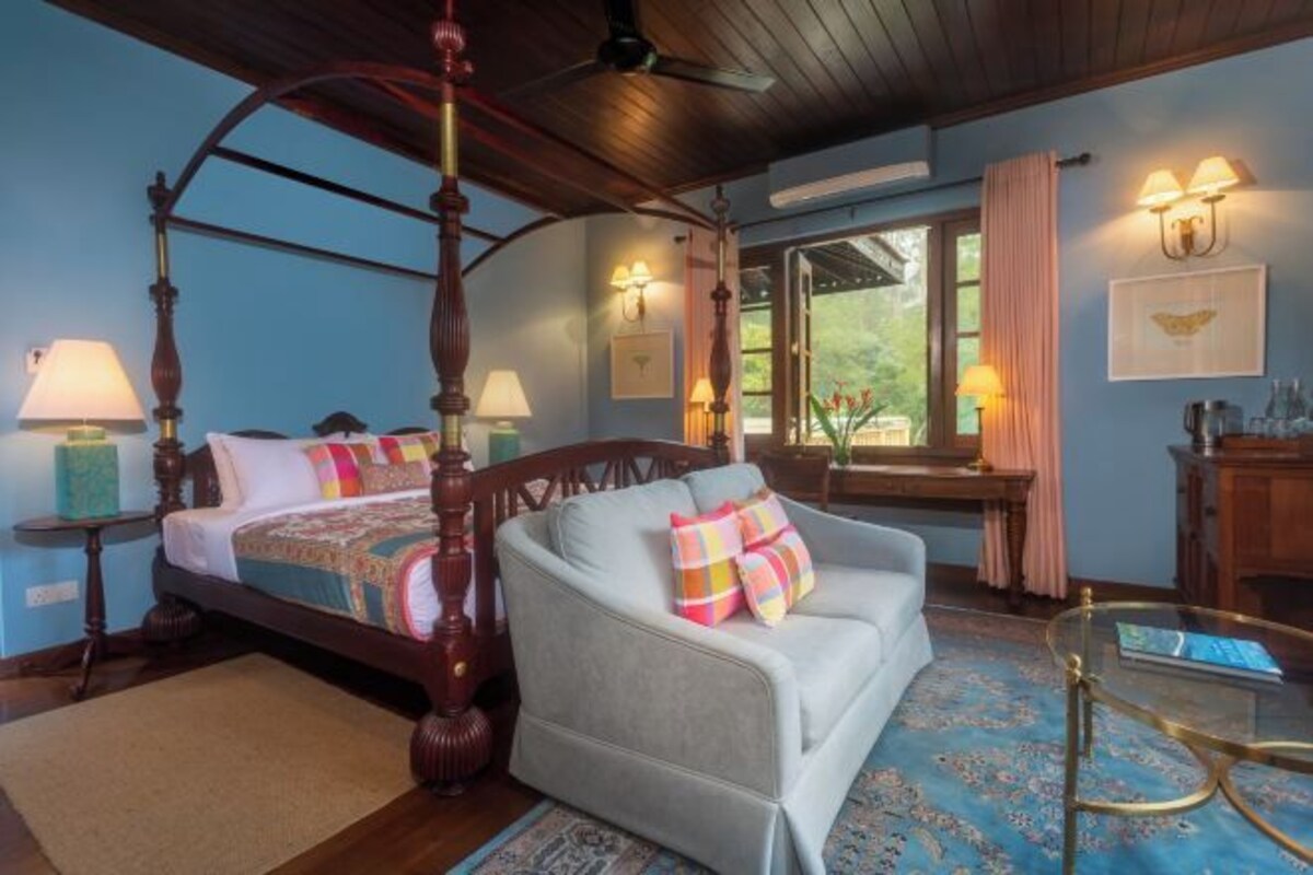 Un dormitorio con cama con dosel, un sofá, una mesa de centro de vidrio y vistas al exterior a través de una ventana.