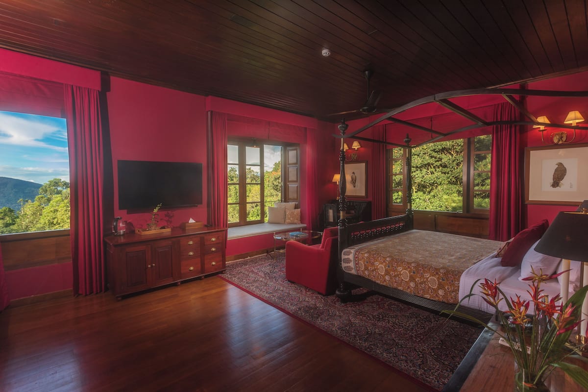 A bedroom with a large bed, a TV, a window seat, and a view of the outdoors.