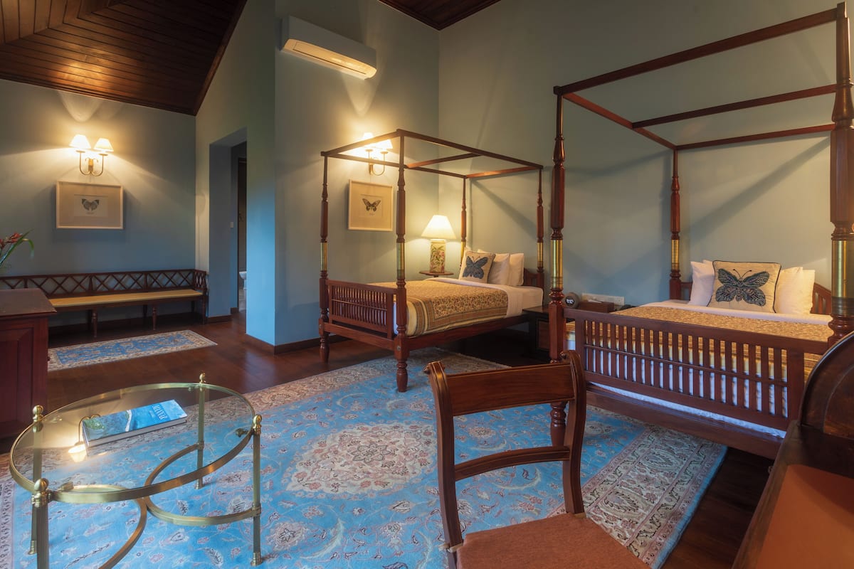 A four-poster bed with a wooden frame and a matching canopy, a glass coffee table, a wooden chair, and a bedside table with a lamp.