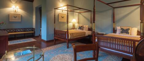 A four-poster bed with a wooden frame and a matching canopy, a glass coffee table, a wooden chair, and a bedside table with a lamp.