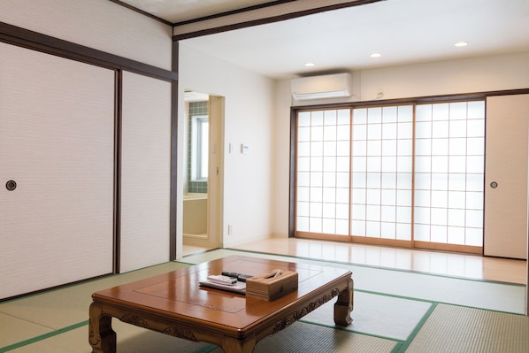 Une pièce de style japonais traditionnel, avec un sol recouvert de tatamis, une table en bois, des portes coulissantes et un appareil de climatisation.