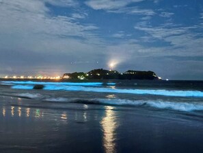 Une plage avec des vagues, une structure illuminée au loin et un ciel nuageux.