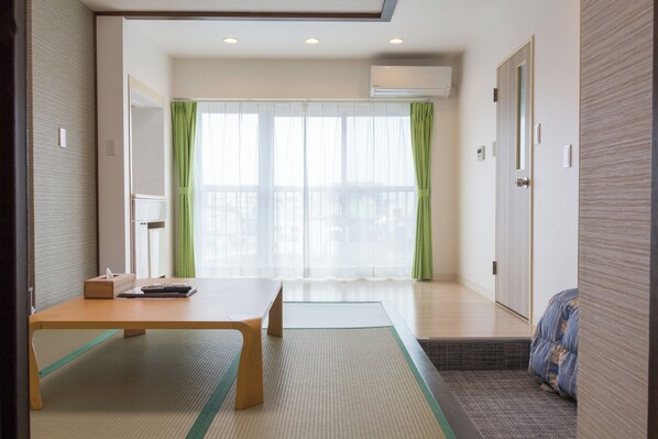 Una habitación con suelo de estera de tatami, una mesa de madera, una cama futón y una puerta corredera.