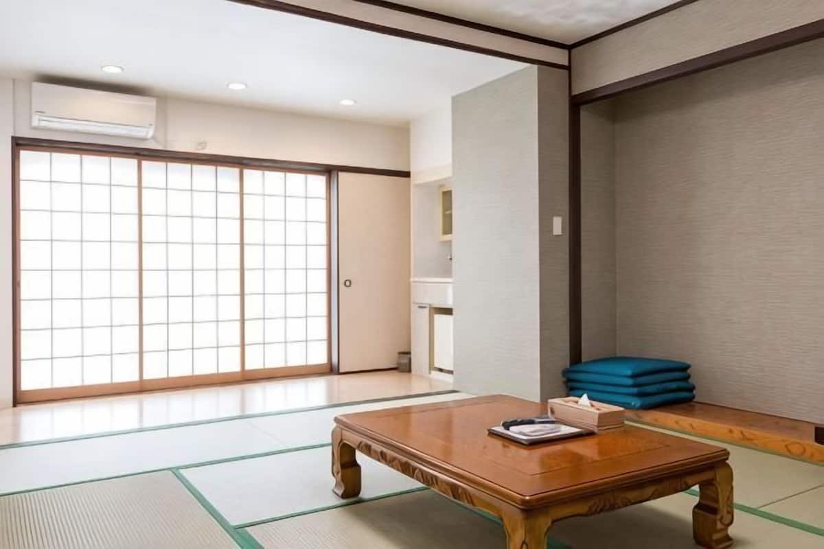 A traditional Japanese room with tatami flooring, a wooden table, sliding doors, and a view of a garden.