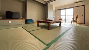A traditional tatami mat room with a wooden table, a television on a shelf, and a sliding door leading to a balcony. - kishu railway katase enoshima hotel (Fujisawa)