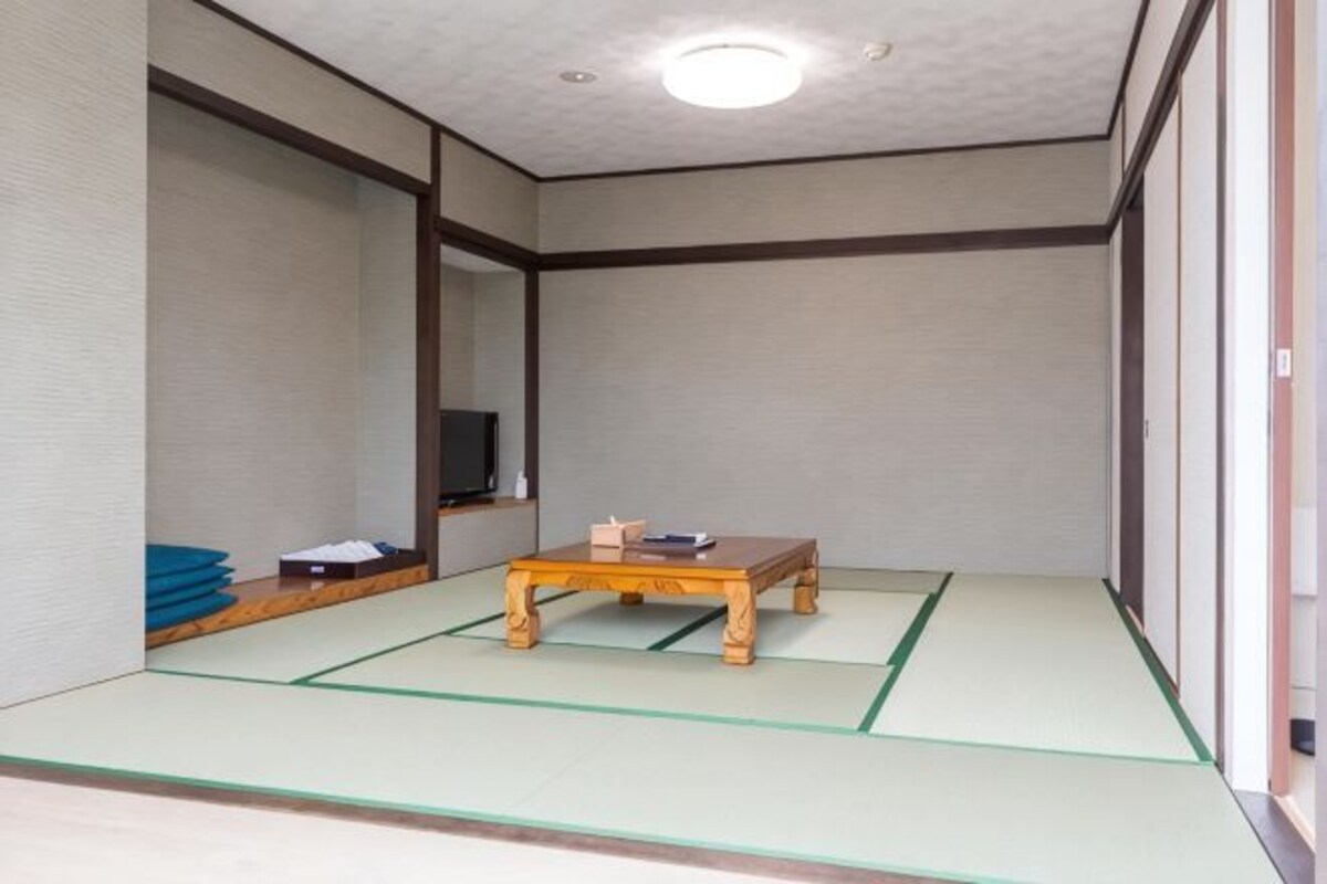 Um quarto japonês tradicional, com tatames, uma mesa de madeira baixa e uma televisão na parede.
