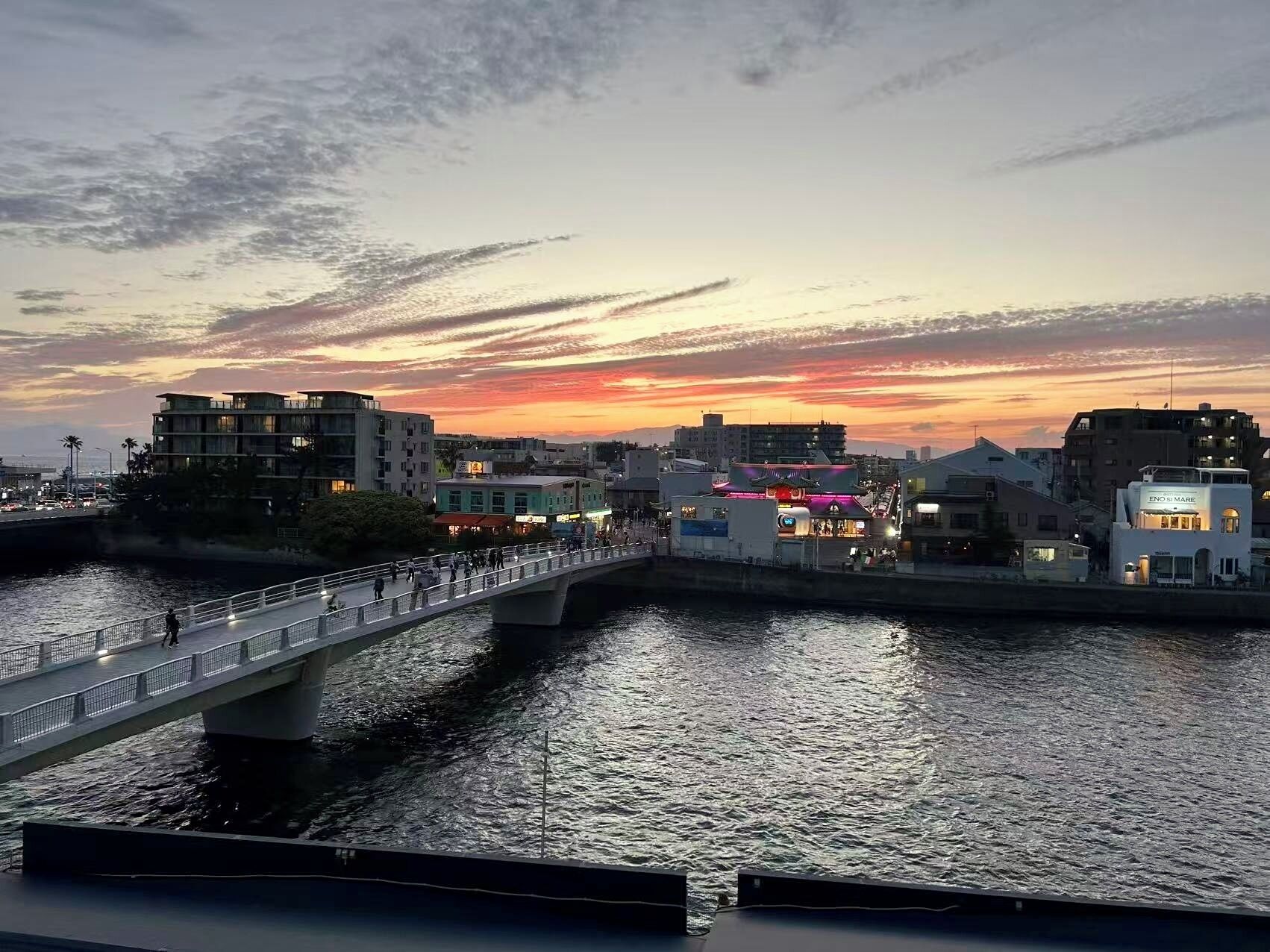 A waterfront bridge with buildings on either side, a clear sky, and calm water.