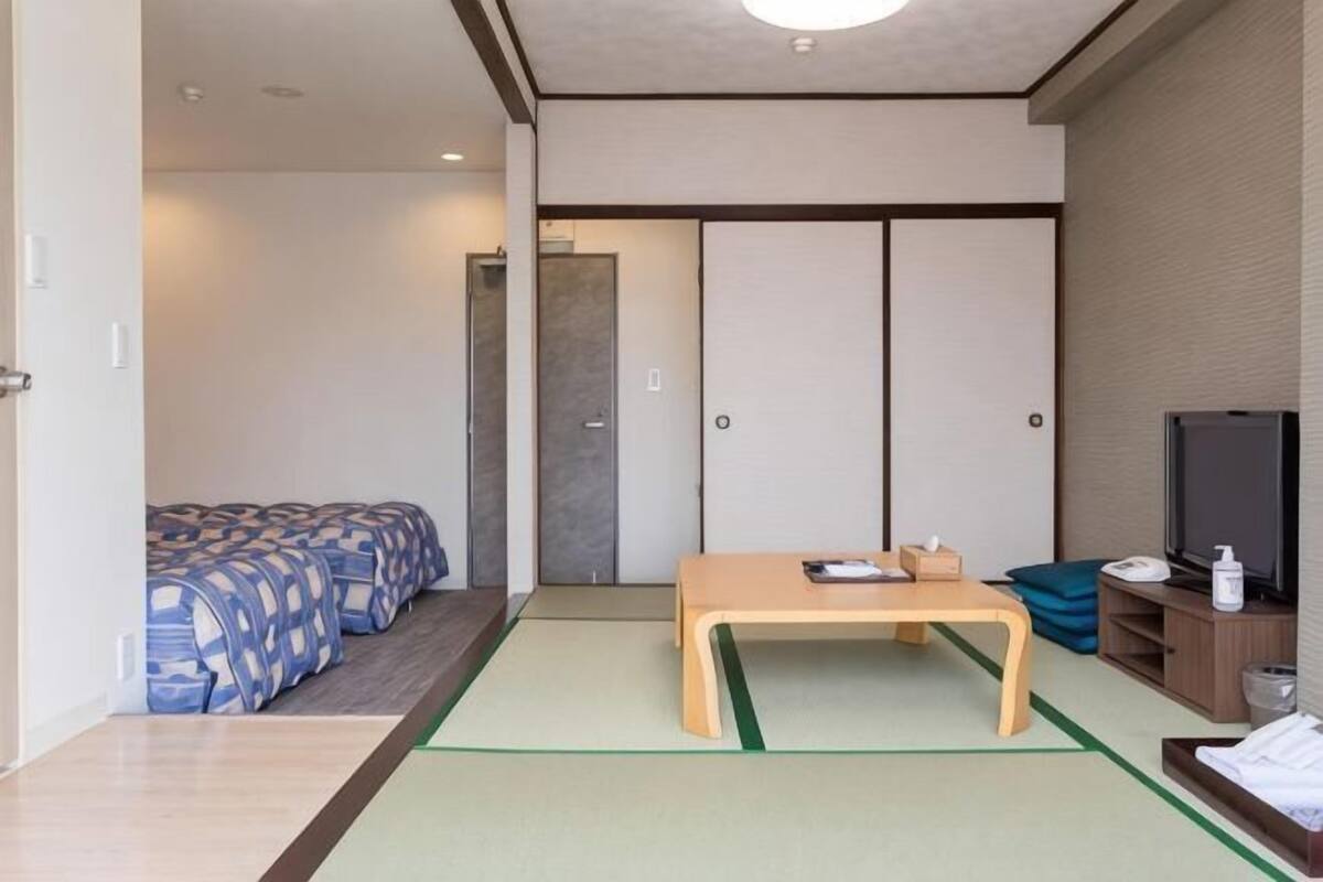 A room with a futon bed, a wooden table, a television, and a sliding door.