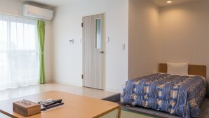 A hotel room with a bed, a table with a tissue box and remote controls, a green curtain, and a door. - kishu railway katase enoshima hotel (Fujisawa)