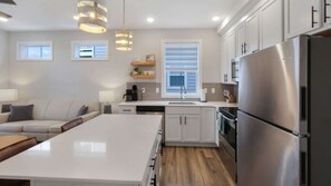 A modern kitchen with a central island, white cabinetry, stainless steel appliances, and pendant lighting.