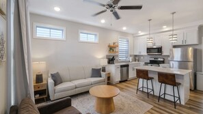 A modern kitchen with white cabinets, a stainless steel refrigerator, and a dining area with a round wooden table and bar stools.