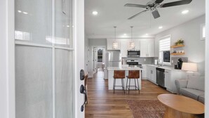 A modern kitchen with white cabinets, stainless steel appliances, and a central island with bar stools. - Mansion Flat @ Navvy Town (Ottawa)
