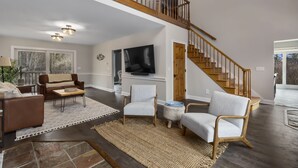 Un salon spacieux avec un haut plafond, un escalier et une grande fenêtre.
