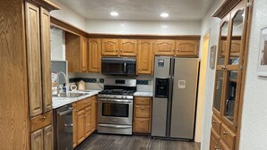 A modern kitchen with wooden cabinets, stainless steel appliances, and a dark wood floor.