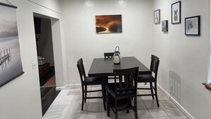 A dining area with a table and chairs, a painting on the wall, and a framed picture.