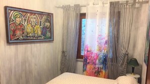 Quarto com cama, quadro, janela com cortinas e abajur.