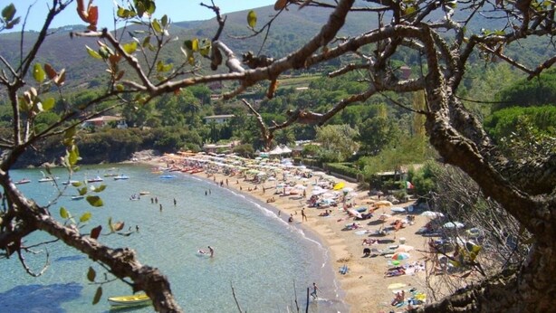 Uma praia com águas cristalinas, guarda-sóis e pessoas.