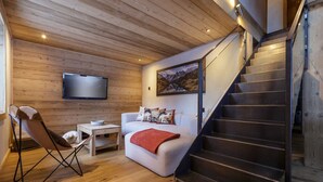 A modern living room with a wooden ceiling, a sofa, a chair, a TV, and a staircase.