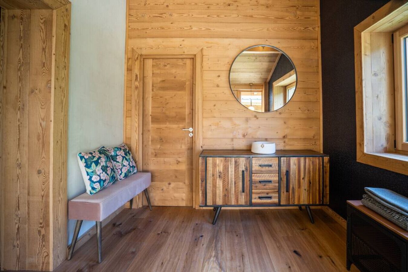 Une pièce en bois avec un banc, une commode à tiroirs et un miroir rond accroché au mur.