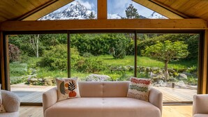 A modern living room with a large window overlooking a lush garden and mountains.