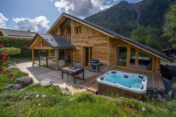 Una cabaña de madera con jacuzzi, terraza y vistas a la montaña.