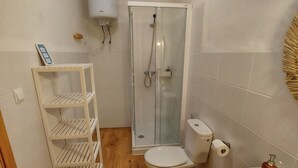 Une petite salle de bain comprenant des toilettes, un lavabo, une douche et une étagère blanche.