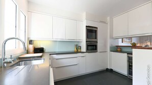 A modern kitchen with white cabinets, stainless steel appliances, and a sleek countertop. - Air-conditioned house, close to beach 9 people  et  mooring (PORT GRIMAUD)