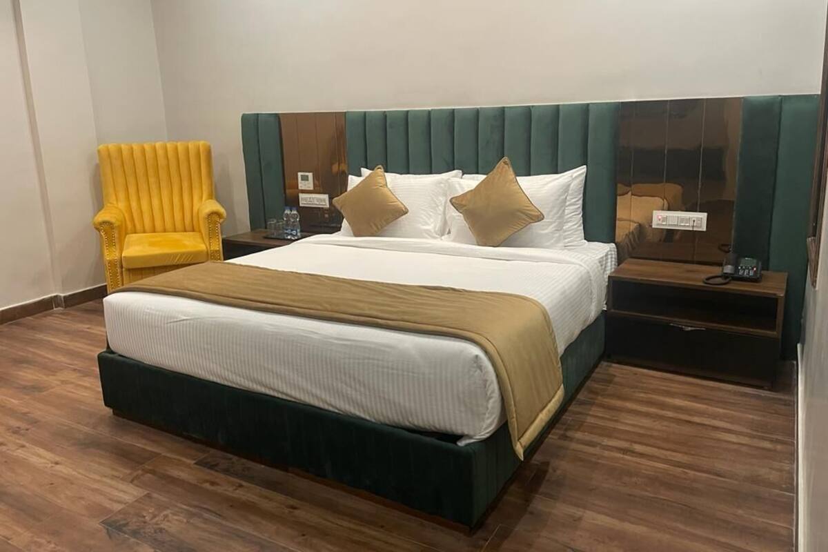 A hotel room with a large bed, a yellow armchair, a wooden nightstand, and a green upholstered headboard.