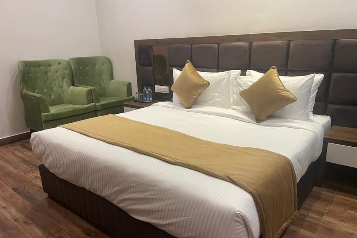 A hotel room with a large bed, a green armchair, and a nightstand with a lamp.