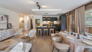 Ein modernes Wohnzimmer mit Essbereich, Küche und Bar. Es gibt verschiedene Sitzgelegenheiten, darunter Barhocker und Stühle.