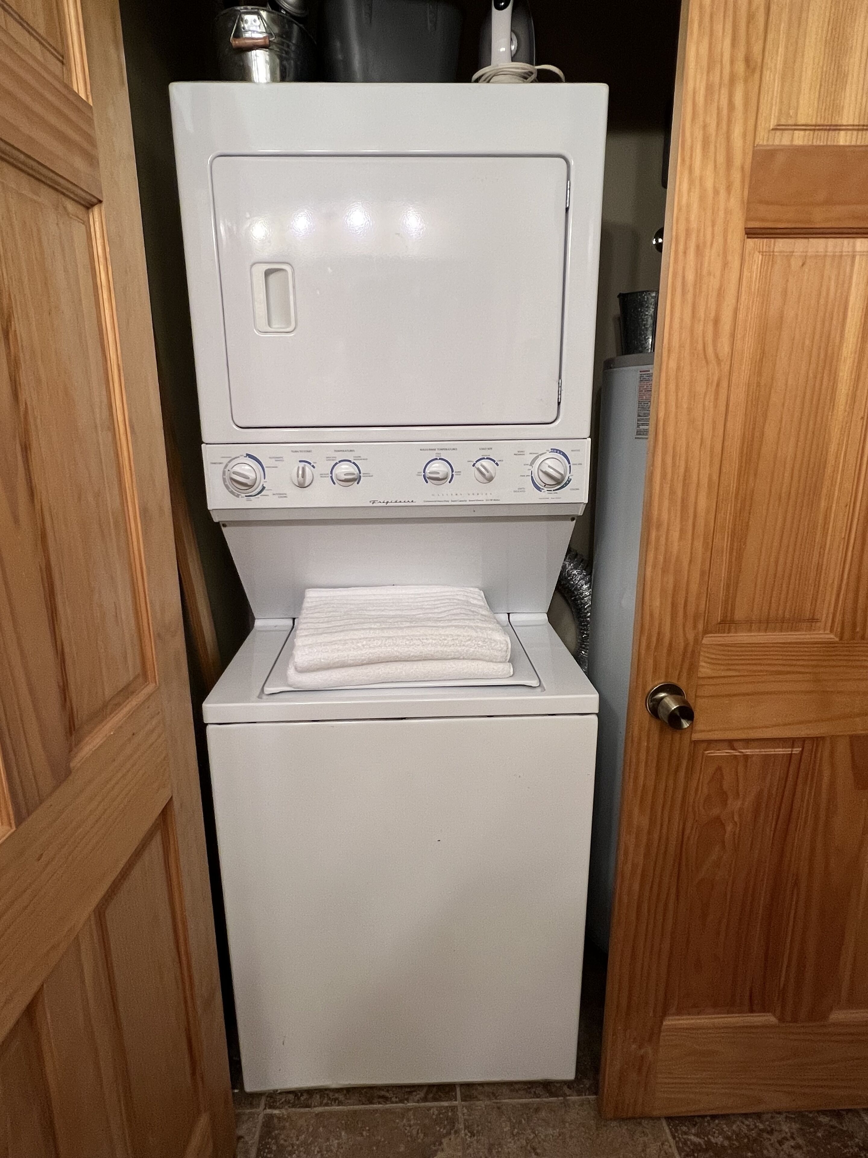 Una màquina de rentar i assecar compacta, de color blanc, amb un quadre de control, situada en un espai de bugaderia amb panells de fusta.