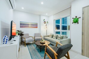 Un soggiorno moderno con un divano, due poltrone, un tavolino, una televisione e un quadro appeso al muro.