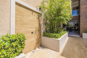 A modern building with a wooden door, a planter with greenery, and a balcony with a railing.