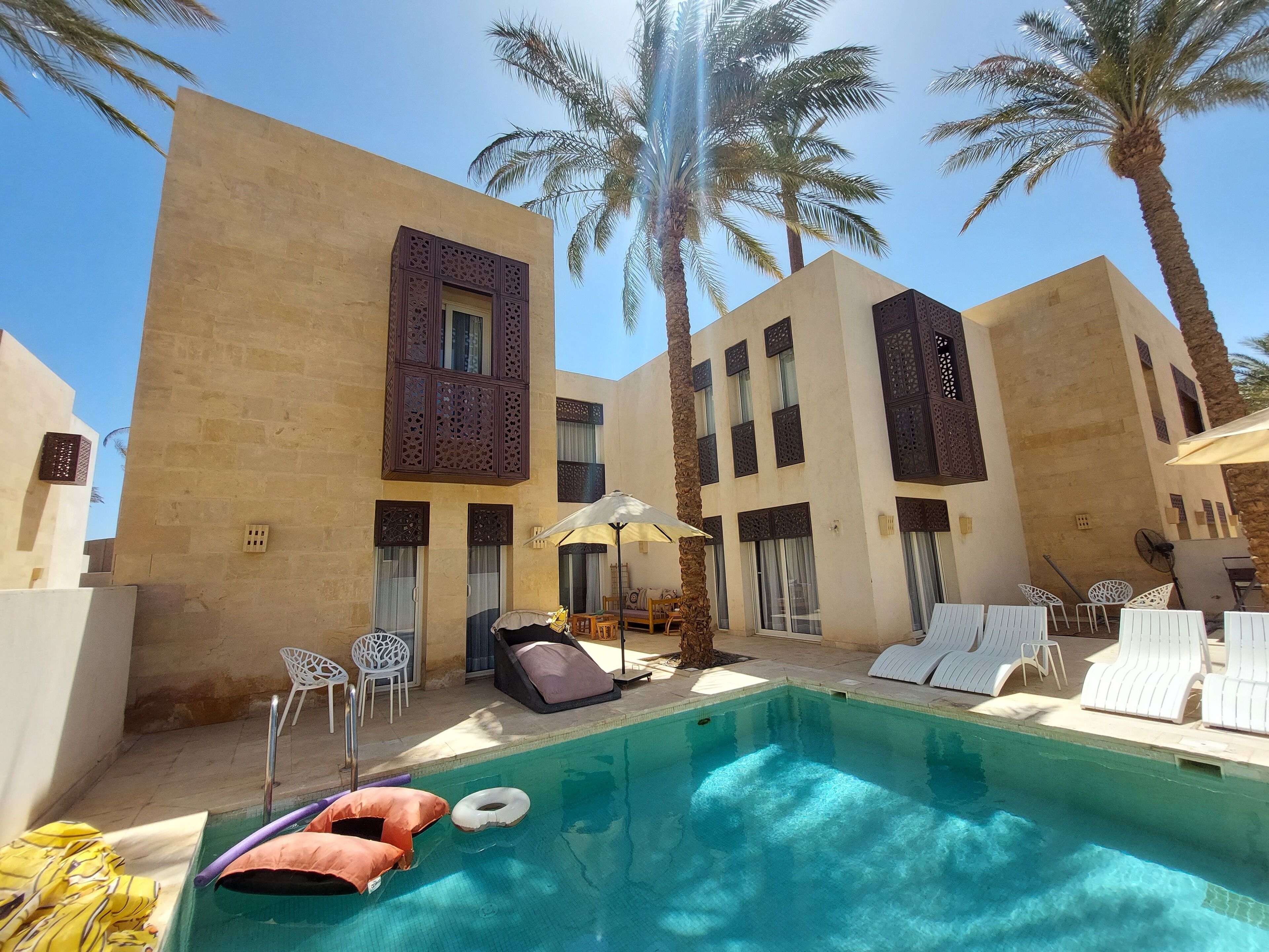 A pool area with lounge chairs, a sunbed, and a small table with chairs.