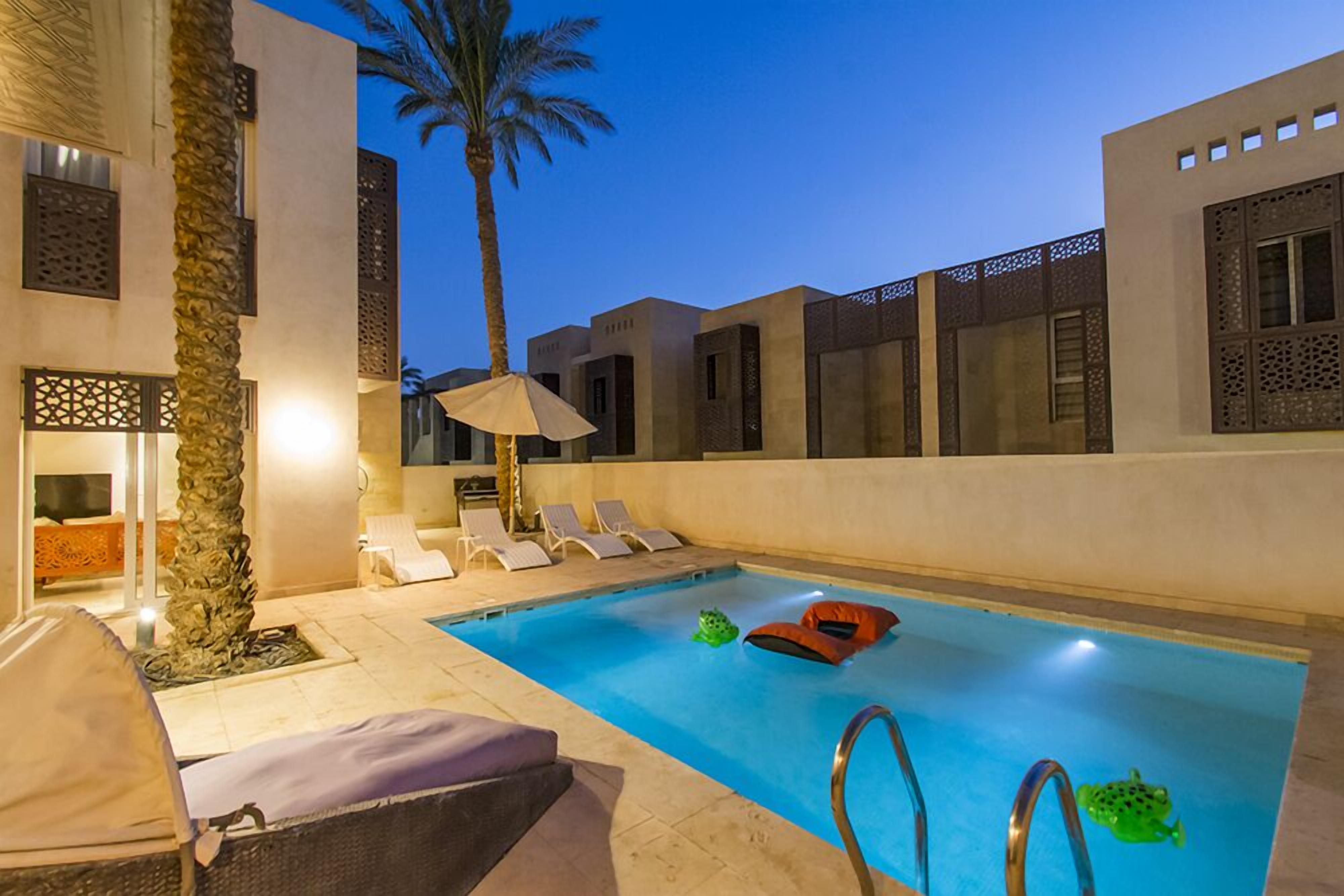 A swimming pool with lounge chairs, a palm tree, and a covered seating area.