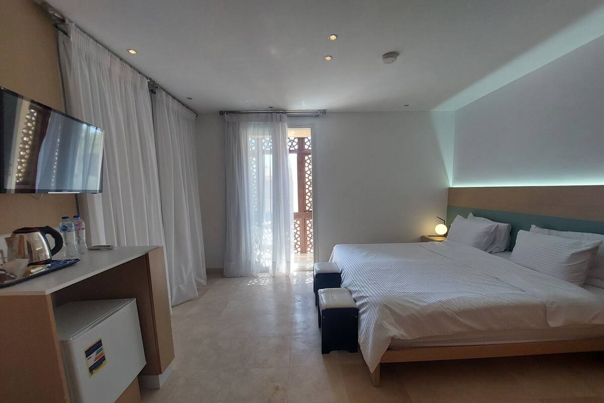 A hotel room with a bed, a desk, a TV, and a window with curtains.