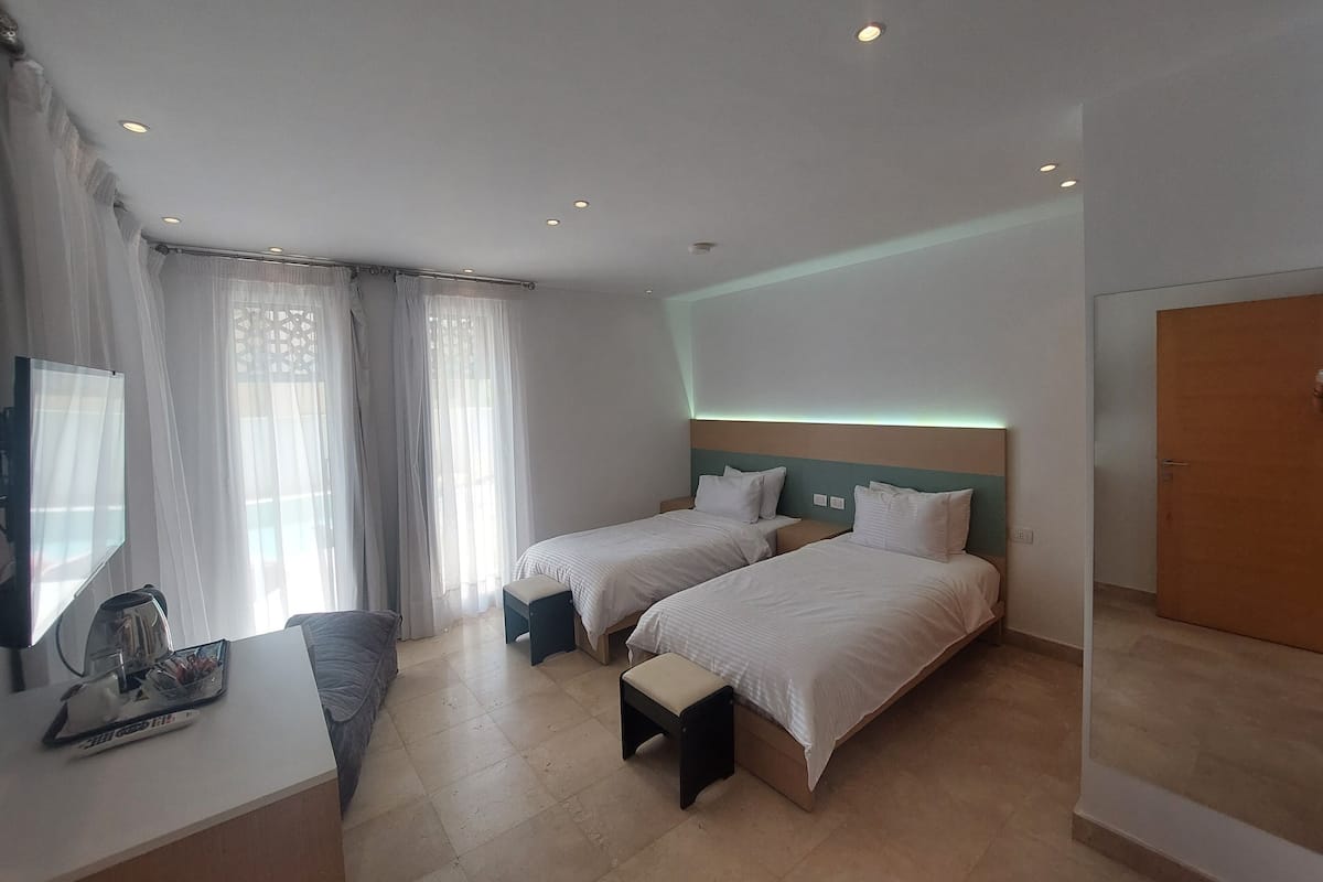A hotel room with two beds, a desk, a TV, and a bathroom door.