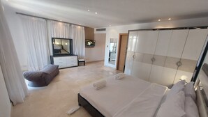 Un dormitorio moderno con una cama grande, un tocador con espejo, un televisor y un armario.