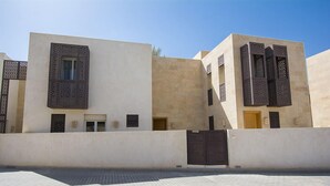 Un edificio moderno con fachada plana, amplias ventanas con diseños de celosía y una entrada protegida por una reja.
