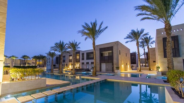 Un hotel moderno con zona de piscina, palmeras y arquitectura contemporánea.