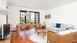 A spacious living area with a dining table, wicker furniture, a sofa, and a television. - Sunset Tirant, Your seaside retreat (Platges de Fornells)