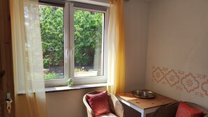 Una habitación con ventana, sillas de mimbre, una mesita y un detalle decorativo en la pared.