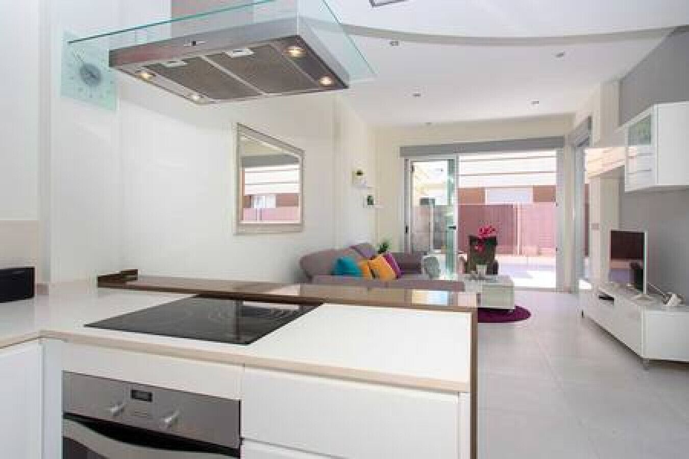 Une cuisine moderne dotée d’un îlot central, un coin repas séparé par une cloison en verre et un espace de vie comprenant un canapé et des éléments de décoration.