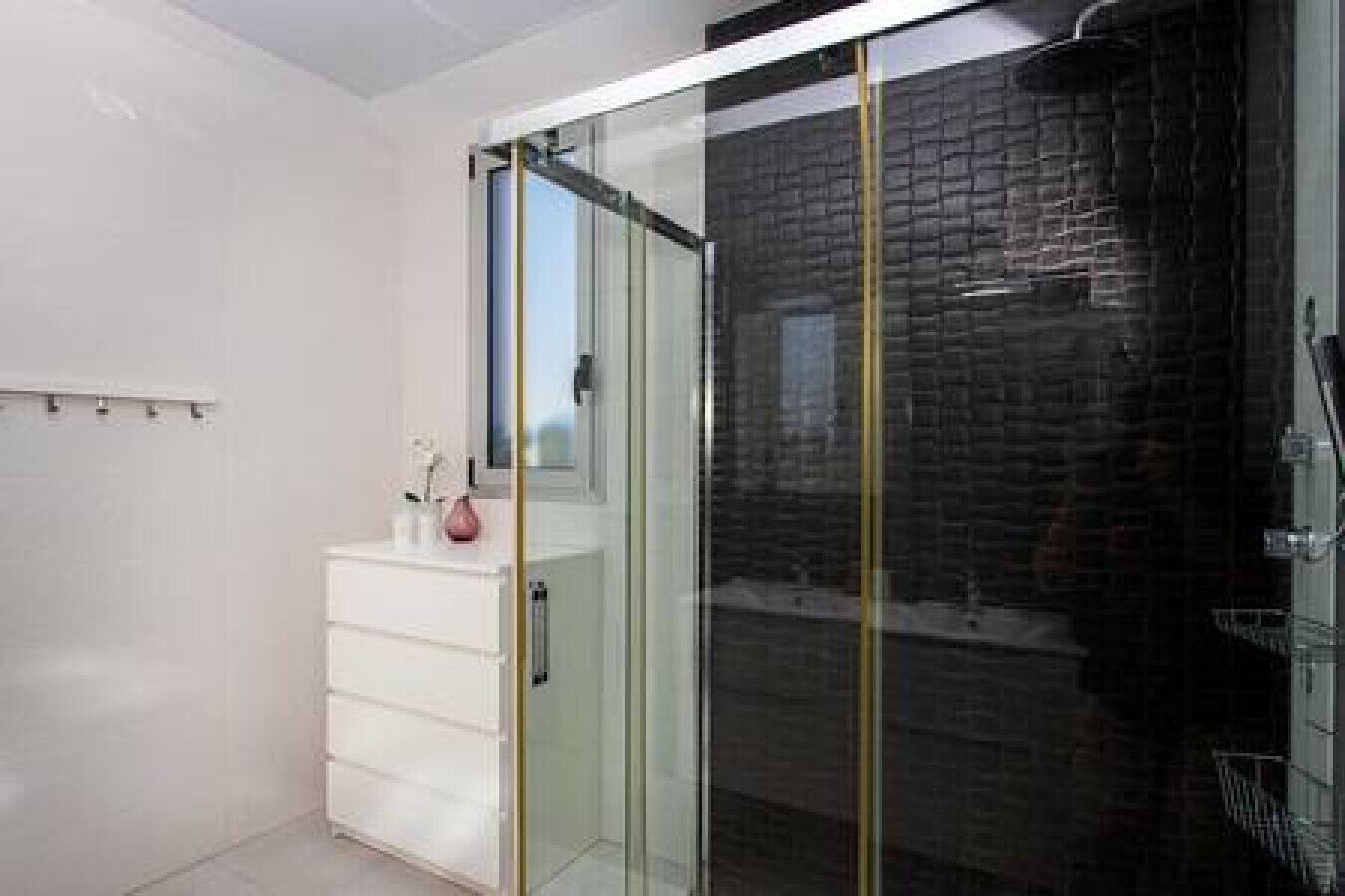 Een moderne badkamer met een glazen douchecabine, een wit wastafelmeubel en een donkere bakstenen muur.