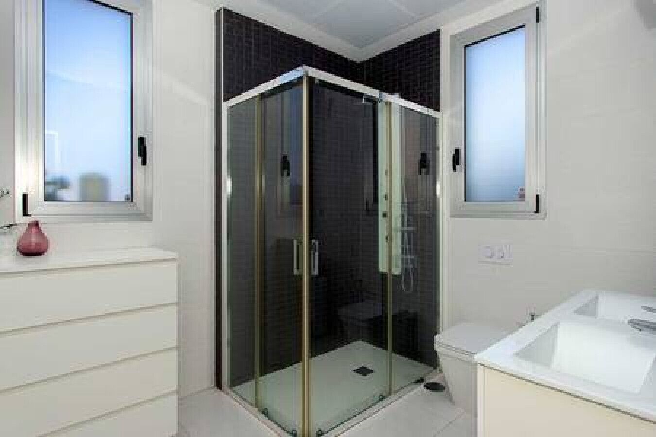 Une salle de bain moderne avec une douche à parois de verre, un lavabo blanc et un vase posé sur le plan de travail.