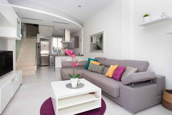 Uma sala de estar moderna com um sofá cinzento, uma mesa de centro branca e uma planta de orquídea rosa.