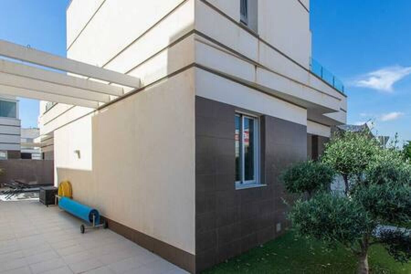 Een modern gebouw met een plat dak, een groot raam en een kleine boom op de voorgrond.
