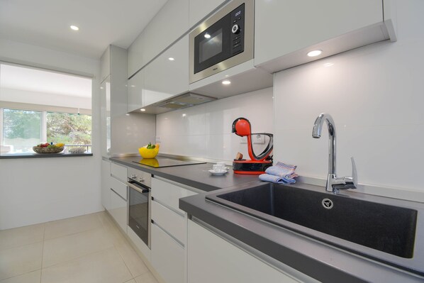 A modern kitchen with a built-in microwave, stainless steel sink, and a window with a view of greenery.