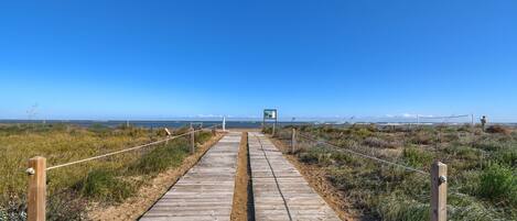 A wooden boardwalk leading to a beach with a sign in the distance.